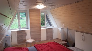 Helle, moderne Dachzimmer mit zwei Fenstern und minimalistischem Mobiliar.